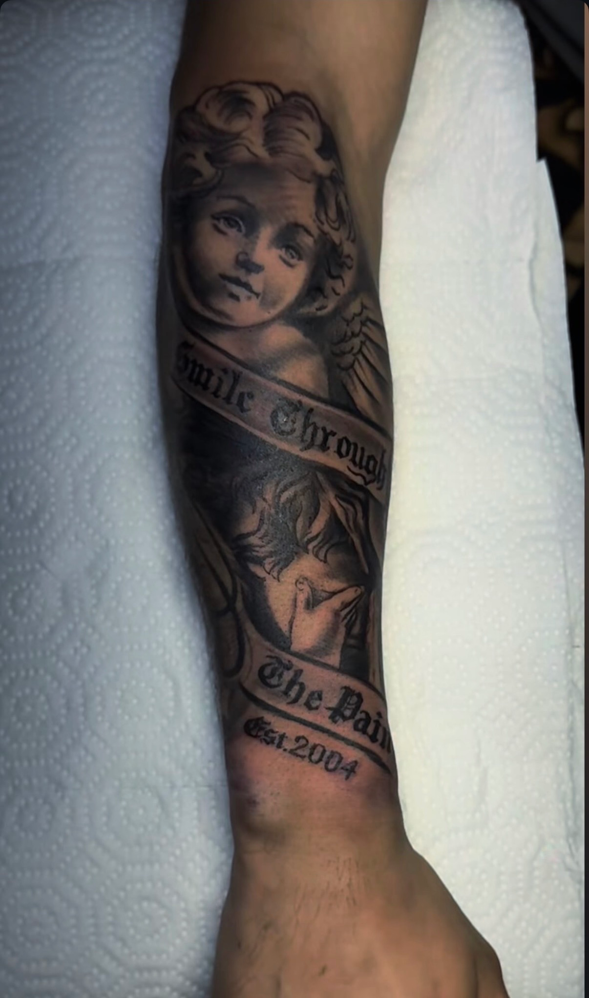 Cherub with smile through the pain lettering forearm tattoo